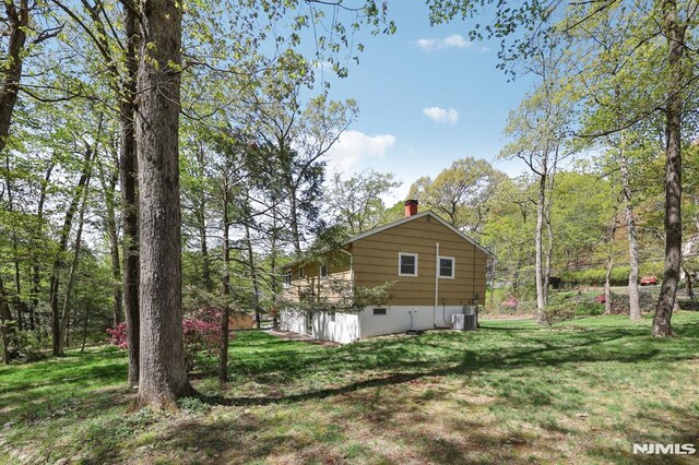 view of side of property with a yard, a chimney, and cooling unit
