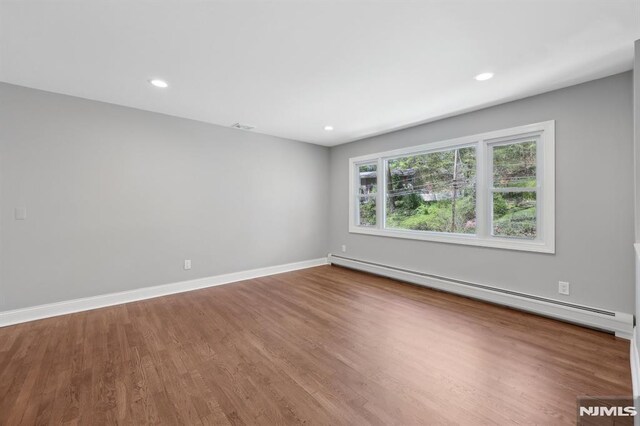 spare room with visible vents, baseboard heating, wood finished floors, baseboards, and recessed lighting