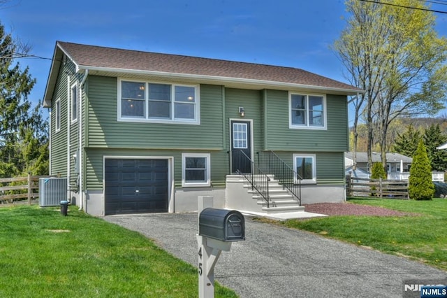 bi-level home featuring driveway, central AC, fence, an attached garage, and a front yard