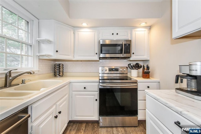 kitchen with white cabinetry, appliances with stainless steel finishes, dark wood-style flooring, a sink, and backsplash