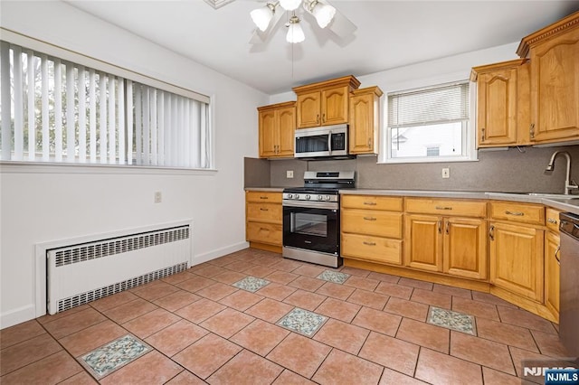 kitchen featuring a sink, tasteful backsplash, radiator heating unit, ceiling fan, and appliances with stainless steel finishes