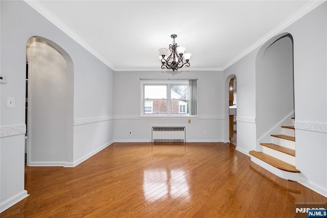 unfurnished dining area with arched walkways, radiator, a chandelier, wood finished floors, and crown molding