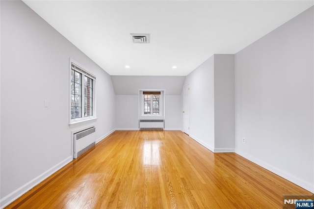 additional living space featuring baseboards, radiator heating unit, light wood-style floors, and visible vents