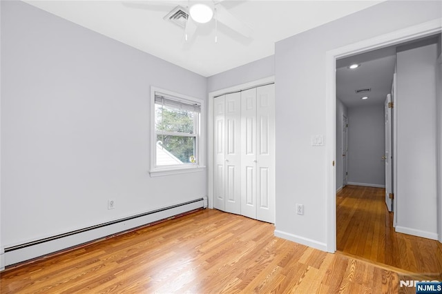 unfurnished bedroom with a baseboard heating unit, light wood-type flooring, baseboards, visible vents, and a closet