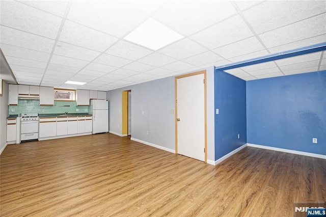 unfurnished living room with baseboards, a sink, light wood-style floors, and a drop ceiling