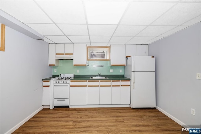 kitchen featuring dark countertops, a sink, white appliances, under cabinet range hood, and a paneled ceiling