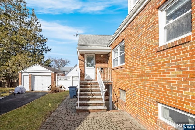 doorway to property featuring a detached garage, driveway, fence, brick siding, and a shingled roof