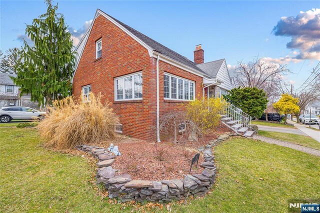 view of property exterior with brick siding, a yard, and a chimney