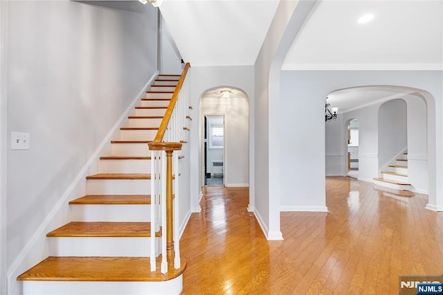 interior space with stairway, arched walkways, crown molding, and light wood-type flooring