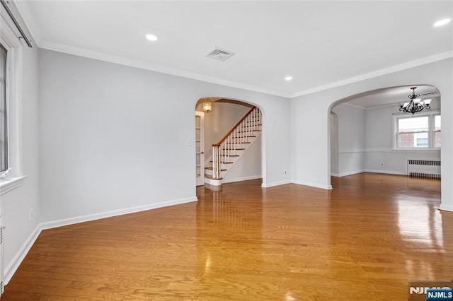 unfurnished room with radiator, arched walkways, visible vents, and light wood finished floors