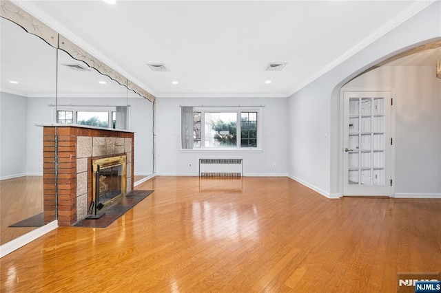 unfurnished living room with radiator, arched walkways, visible vents, and wood-type flooring