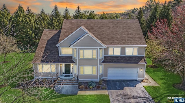 traditional-style house with an attached garage, a shingled roof, a yard, and driveway
