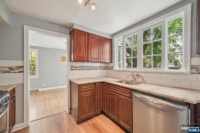 kitchen with stainless steel appliances, a sink, light wood finished floors, backsplash, and light stone counters
