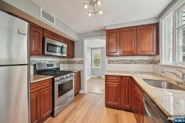 kitchen featuring stainless steel appliances, a sink, light wood-style floors, light stone counters, and baseboards