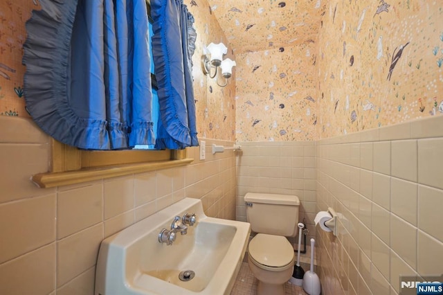 half bath featuring a sink, wainscoting, tile walls, and toilet