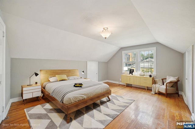 bedroom with light wood-style flooring, lofted ceiling, and baseboards