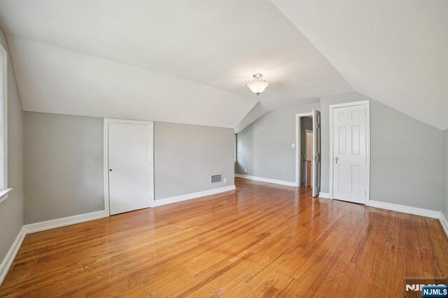 additional living space featuring light wood-type flooring, lofted ceiling, and baseboards
