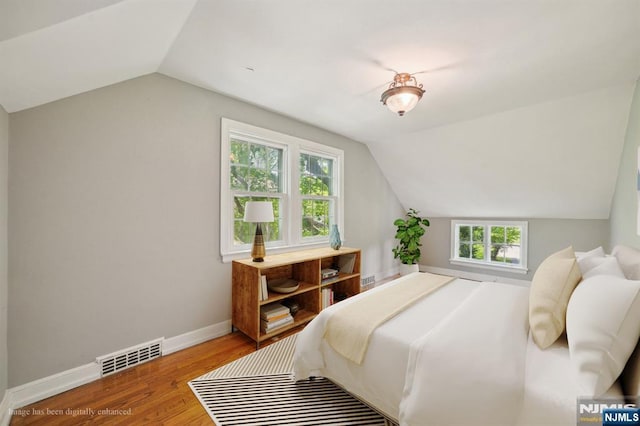 bedroom with vaulted ceiling, wood finished floors, and baseboards