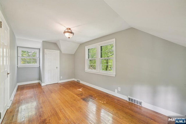 additional living space featuring lofted ceiling, light wood-type flooring, baseboards, and healthy amount of natural light