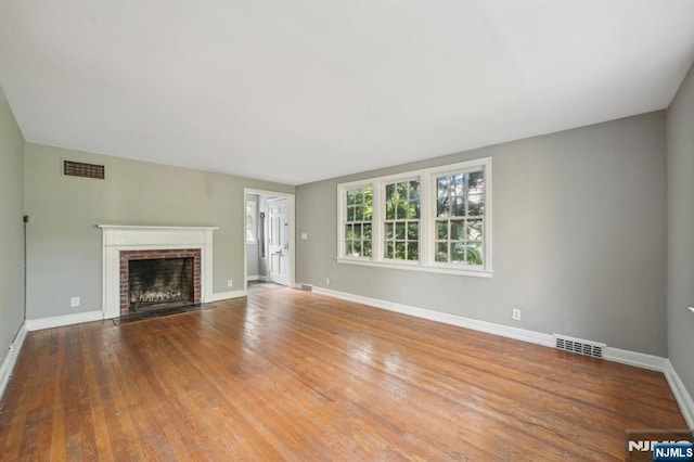 unfurnished living room with a brick fireplace, baseboards, and wood finished floors
