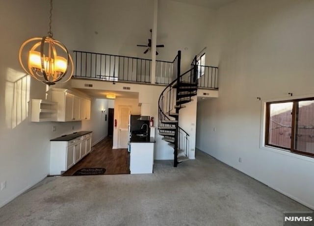 interior space with dark carpet, stairway, a towering ceiling, and ceiling fan with notable chandelier