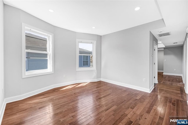 spare room featuring wood-type flooring, visible vents, and baseboards