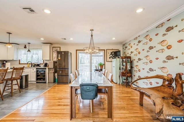 dining area featuring visible vents, an inviting chandelier, crown molding, light wood finished floors, and beverage cooler