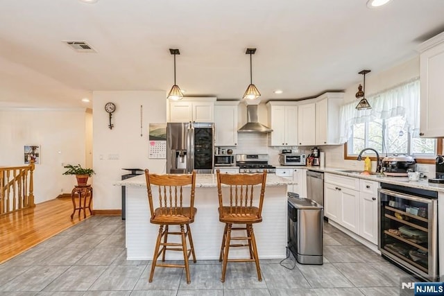 kitchen featuring a center island, wall chimney exhaust hood, a sink, stainless steel appliances, and beverage cooler