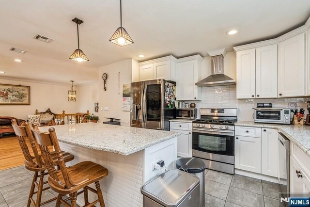 kitchen featuring white cabinets, wall chimney range hood, a kitchen breakfast bar, stainless steel appliances, and a toaster