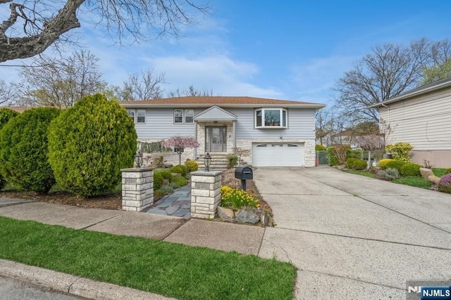 bi-level home with an attached garage, stone siding, and driveway