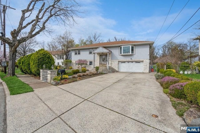 raised ranch featuring an attached garage, driveway, and stone siding
