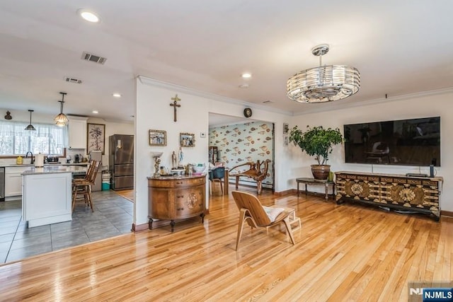 living area with light wood-style floors, recessed lighting, visible vents, and ornamental molding