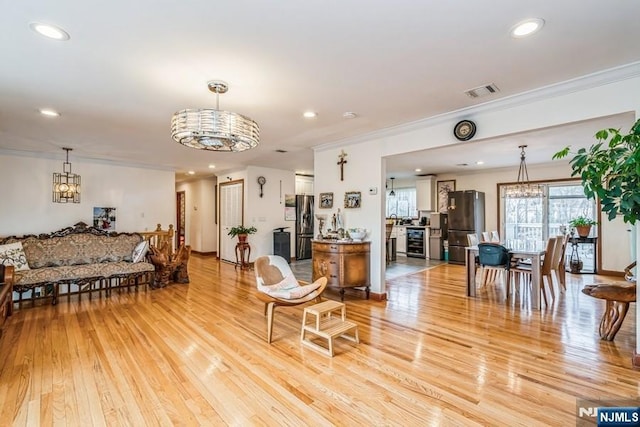 living room with a chandelier, light wood-type flooring, and ornamental molding