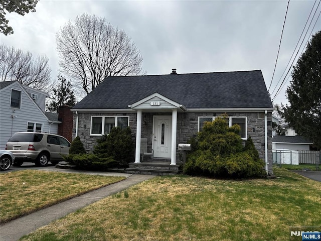 view of front of house featuring a front lawn, a shingled roof, stone siding, and fence