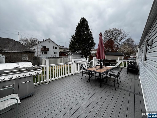 deck featuring outdoor dining space, a grill, an outbuilding, fence, and a storage unit