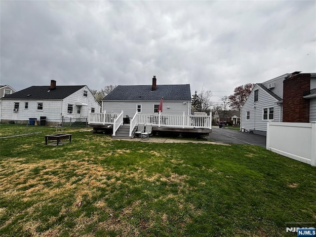 back of property featuring a deck, a chimney, fence, and a lawn