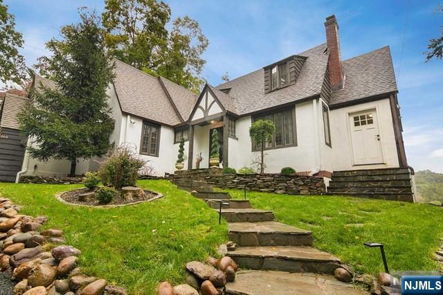 rear view of house with a chimney, a shingled roof, stucco siding, and a lawn