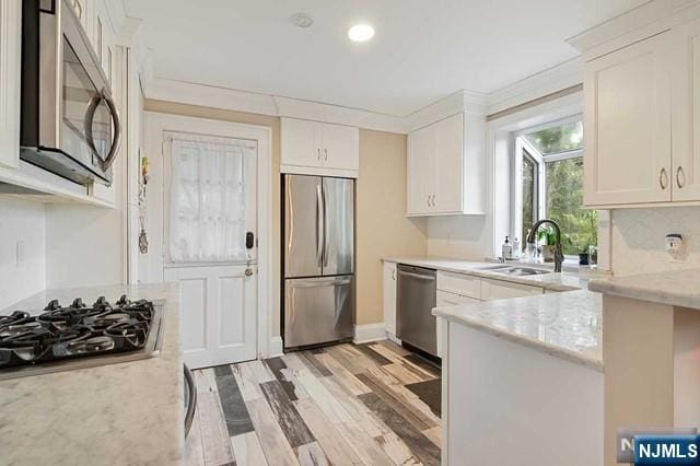 kitchen with a peninsula, white cabinetry, a sink, and appliances with stainless steel finishes