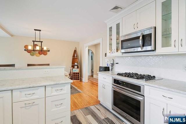 kitchen with light wood-type flooring, white cabinetry, decorative light fixtures, visible vents, and stainless steel appliances