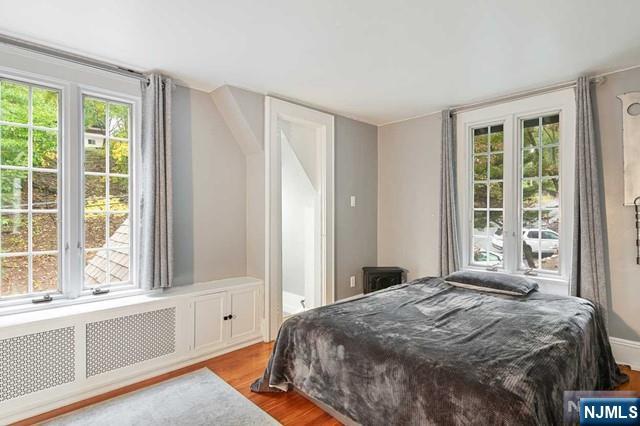 bedroom featuring wood finished floors, radiator heating unit, and multiple windows