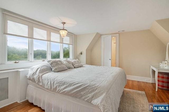 bedroom featuring lofted ceiling, visible vents, baseboards, and wood finished floors