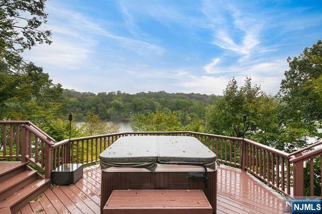 wooden deck with a water view, a hot tub, and a wooded view