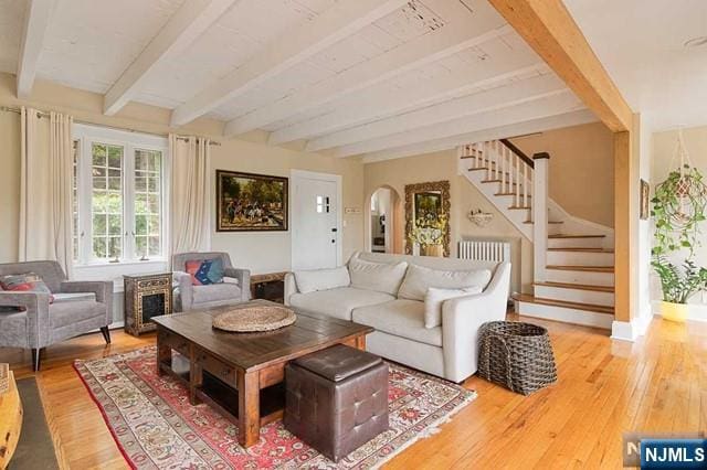 living room featuring arched walkways, beamed ceiling, wood-type flooring, and stairway