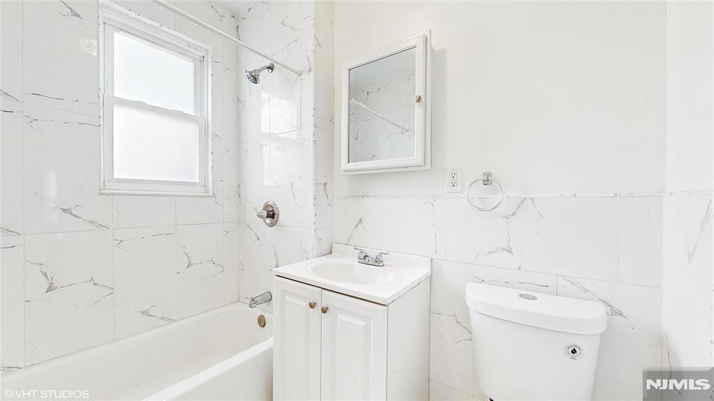 full bathroom featuring bathtub / shower combination, tile walls, vanity, and toilet