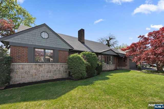 rear view of property featuring stone siding, a lawn, and a chimney
