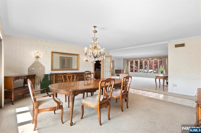 dining space with wallpapered walls, wainscoting, a chandelier, light colored carpet, and ornamental molding
