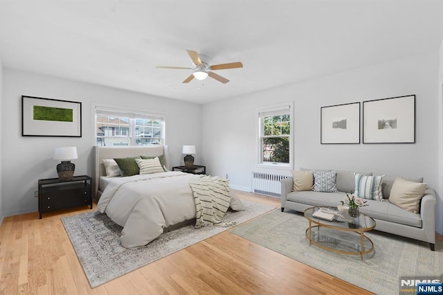 bedroom featuring radiator heating unit, a ceiling fan, wood finished floors, and multiple windows