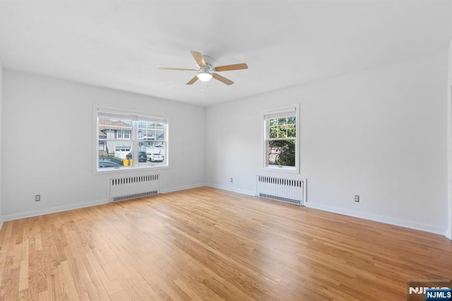 unfurnished room featuring radiator heating unit, a ceiling fan, baseboards, and light wood-type flooring