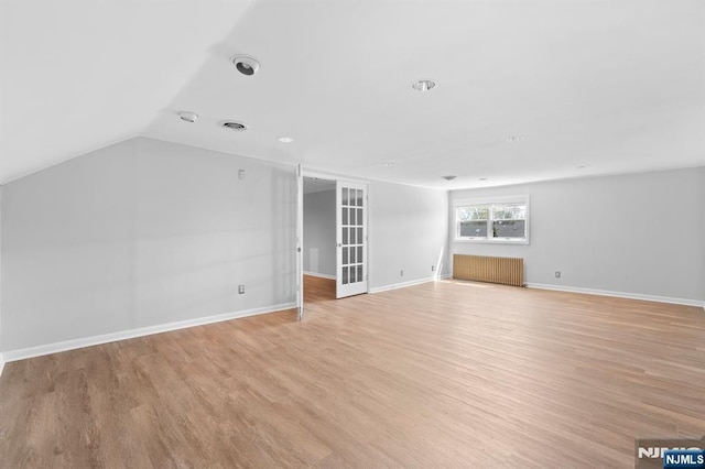 unfurnished living room with light wood-style flooring, radiator, baseboards, visible vents, and lofted ceiling