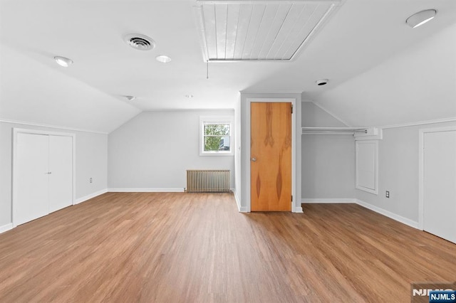 bonus room featuring lofted ceiling, radiator heating unit, light wood finished floors, visible vents, and attic access
